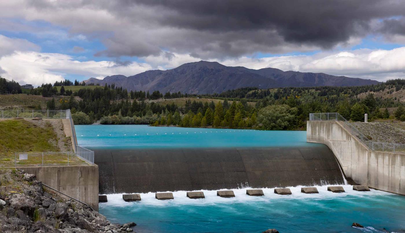 Hydro dam with mountain backdrop and cloudy sky
