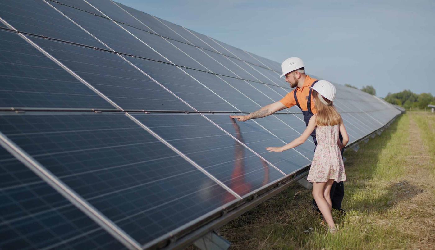 Man and child wearing hard hats touching solar panels in solar farm