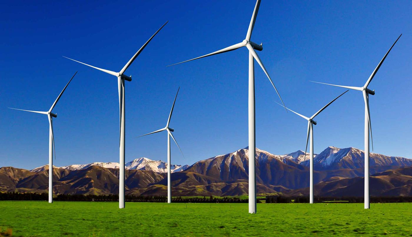 Wind turbines in a field against a mountain backdrop with sunny sky 