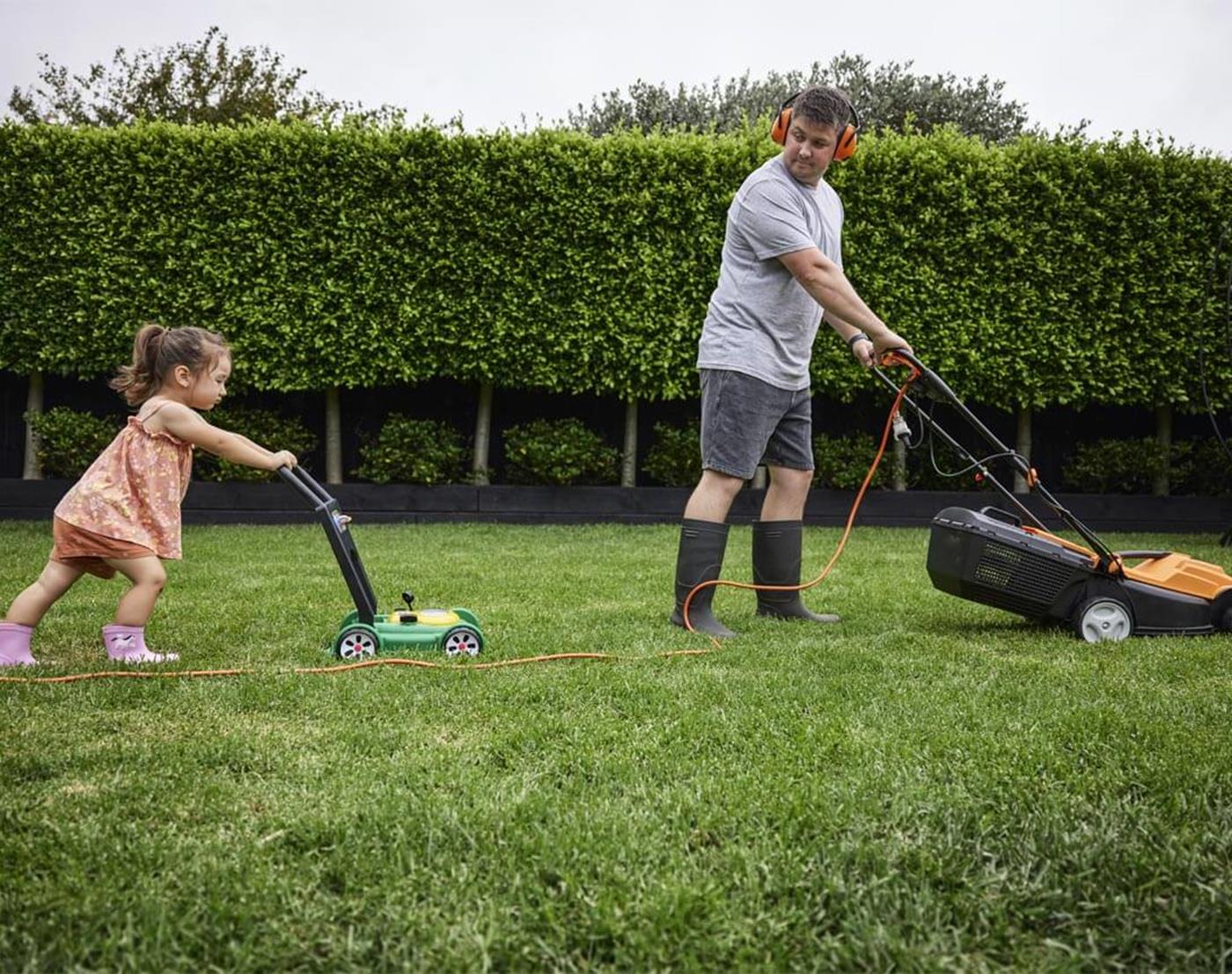 Father and daughter mowing the lawn together with electric mower