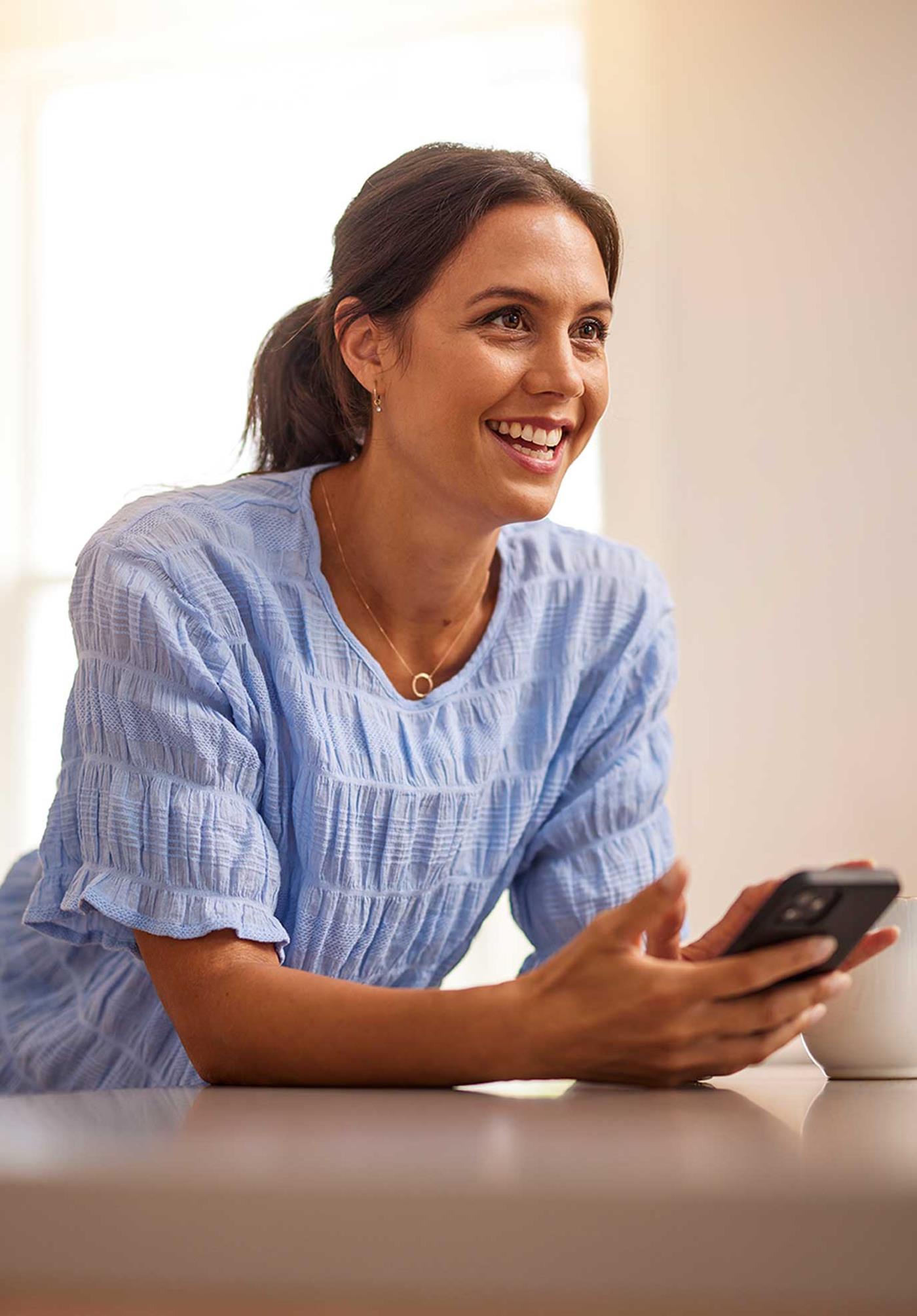 Woman leaning on kitchen bench using Energy IQ app on mobile