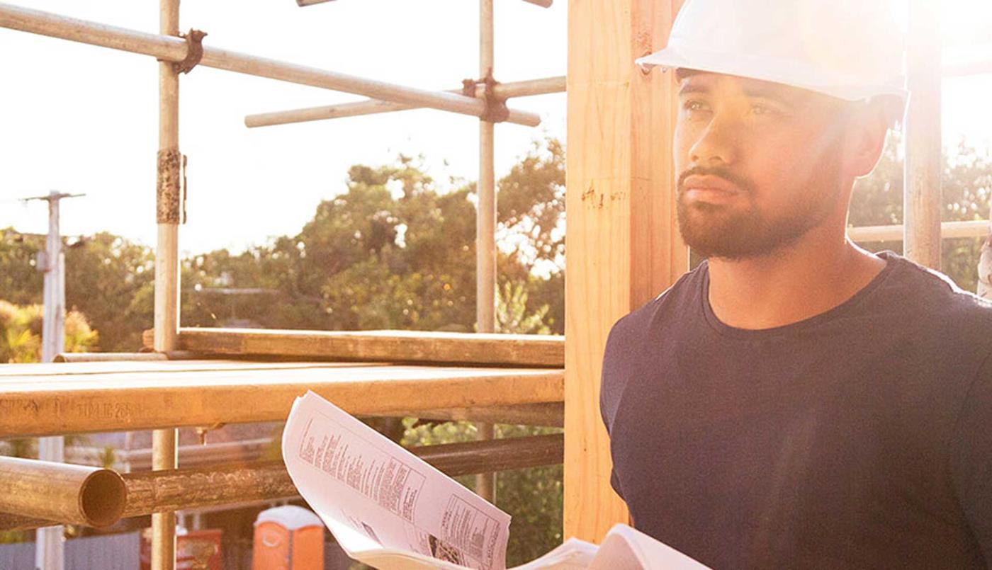 Man in hard hat on building site looking at plans