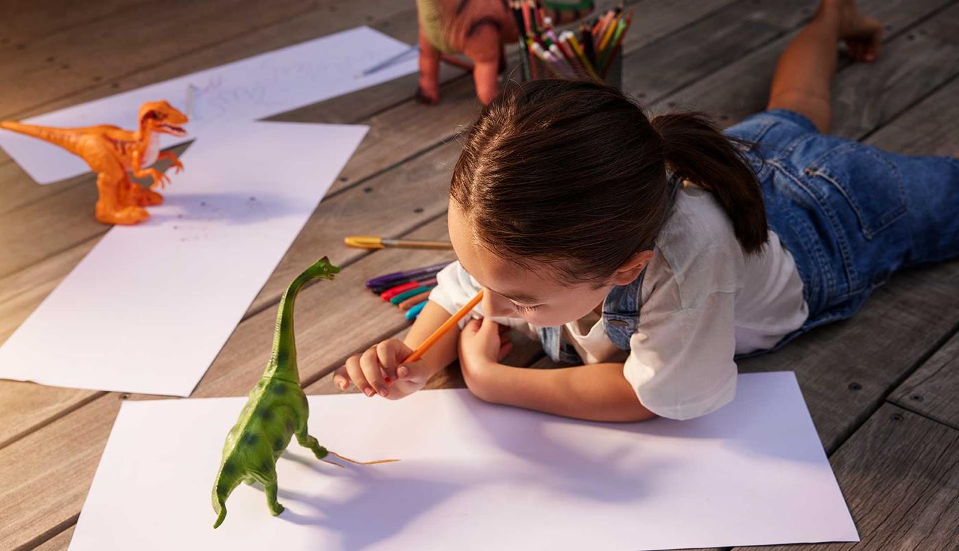 Young girl drawing with toy dinosaurs